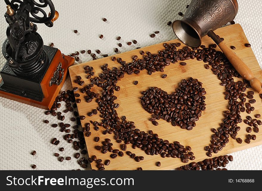 Coffee beans in a heart's shape on the breadboard with coffee mill and coffee pot