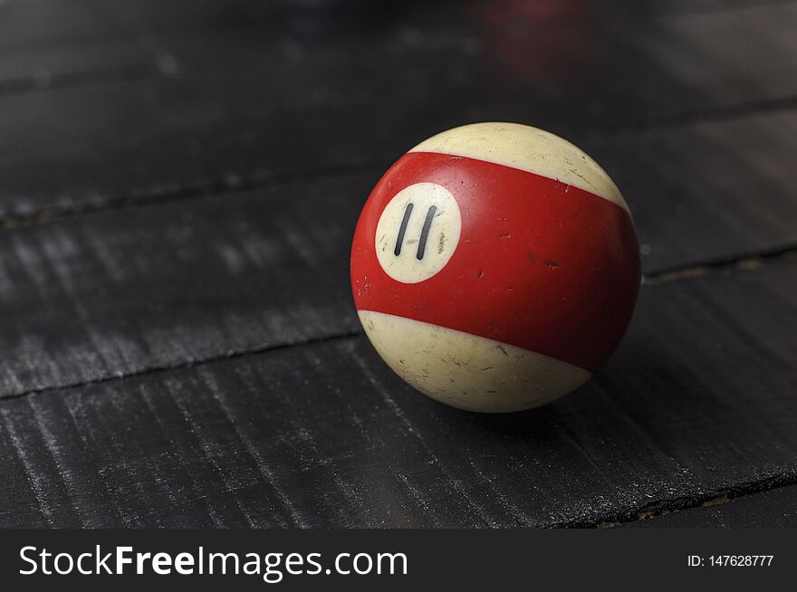 Old billiard ball number 11 striped white and red on black wooden table background, copy space