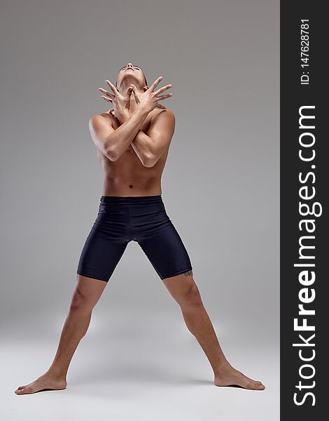 Photo Of A Handsome Man Ballet Dancer, Dressed In A Black Shorts, Making A Dance Element Against A Gray Background In