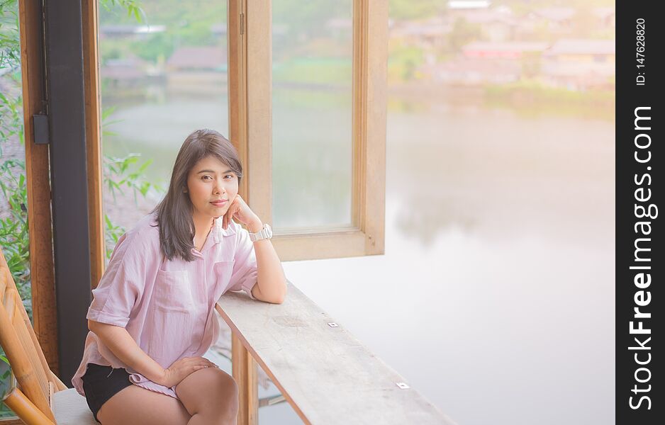 Portrait of Beautiful Asian Woman. Sitting on Wooden chair. Table near the window.