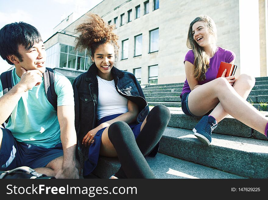 Cute group of teenages at the building of university with books huggings, diversity nations real students lifestyle closeup