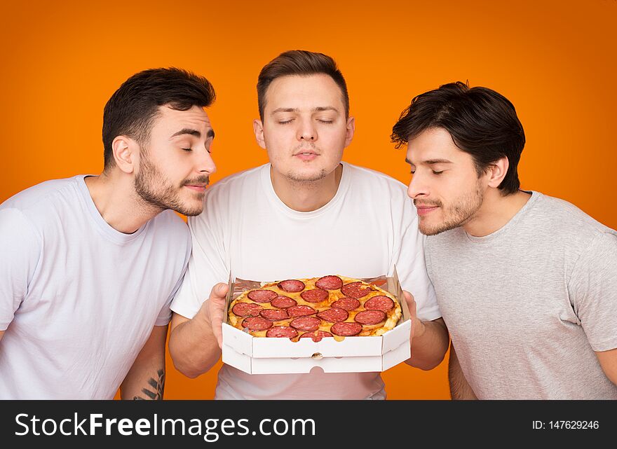 Three Men Smelling Hot Pizza Over Orange Background