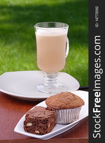 Chocolate brownie, bran muffin and iced cafe au lait on backyard tabletop. Chocolate brownie, bran muffin and iced cafe au lait on backyard tabletop