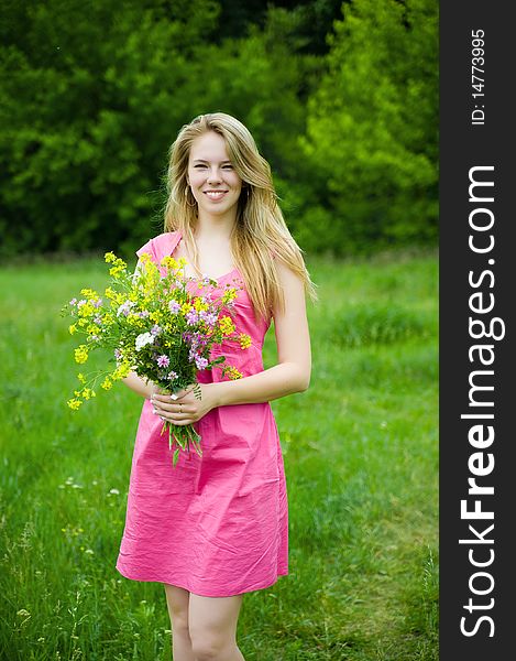 Pretty woman with bouquet of flowers on a meadow