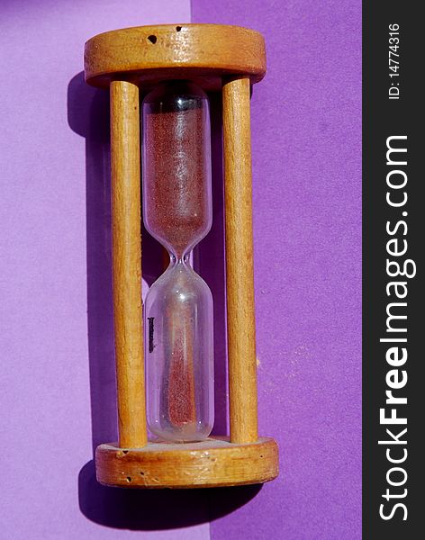 An old style wooden hourglass on a purple background