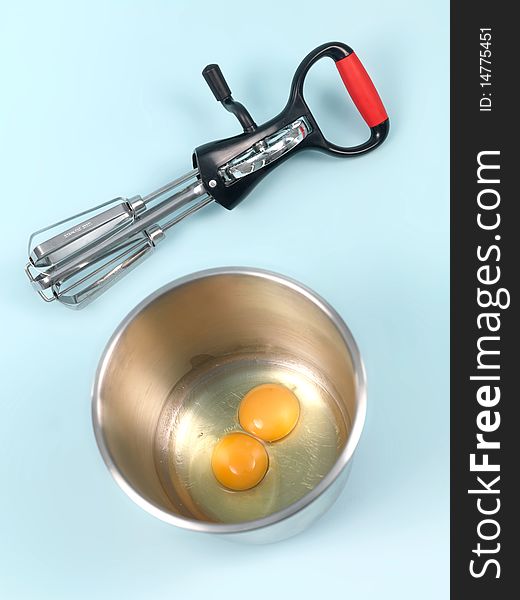 An egg beater eggs and a mixing bowl on a kitchen bench