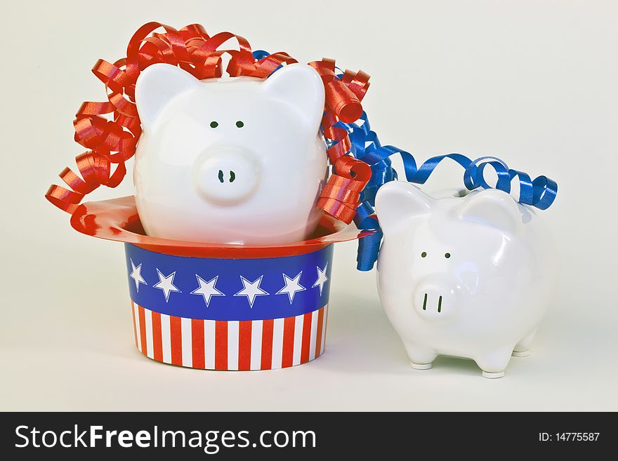 Two patriotic piggy banks, one sitting in a stars and stripes hat, with red and blue ribbon curls on a white background.