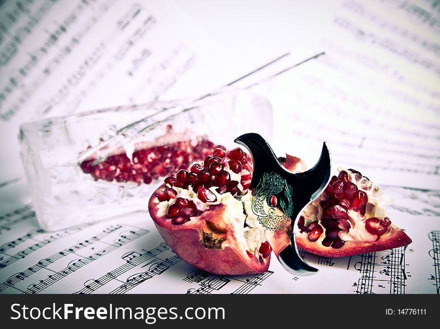 Red pomegranate pierced by shuriken on the music partiture sheets with the metal chopsticks and pomegranate grains in the ice vase. Red pomegranate pierced by shuriken on the music partiture sheets with the metal chopsticks and pomegranate grains in the ice vase