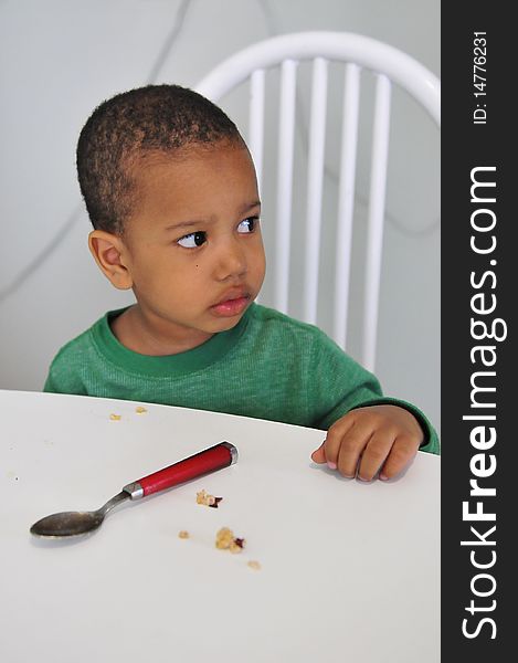 Child looking for more food while sitting at dinner table with spoon ready. Child looking for more food while sitting at dinner table with spoon ready