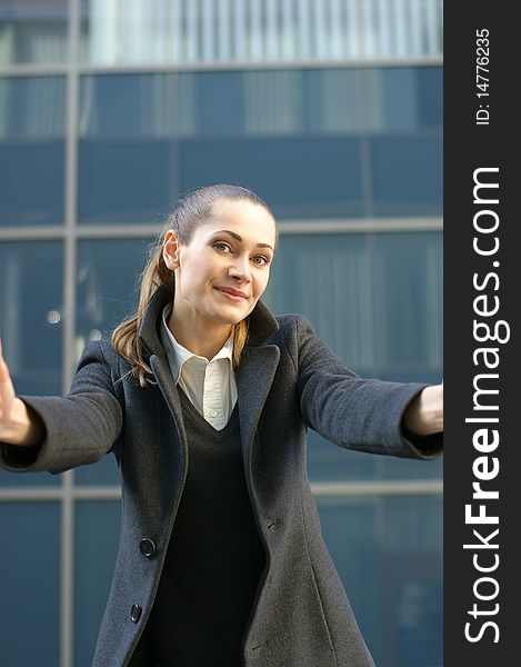 A young and attractive business woman in formal clothes is trying to embrace the camera man. The image is taken on a modern outdoor background. A young and attractive business woman in formal clothes is trying to embrace the camera man. The image is taken on a modern outdoor background.