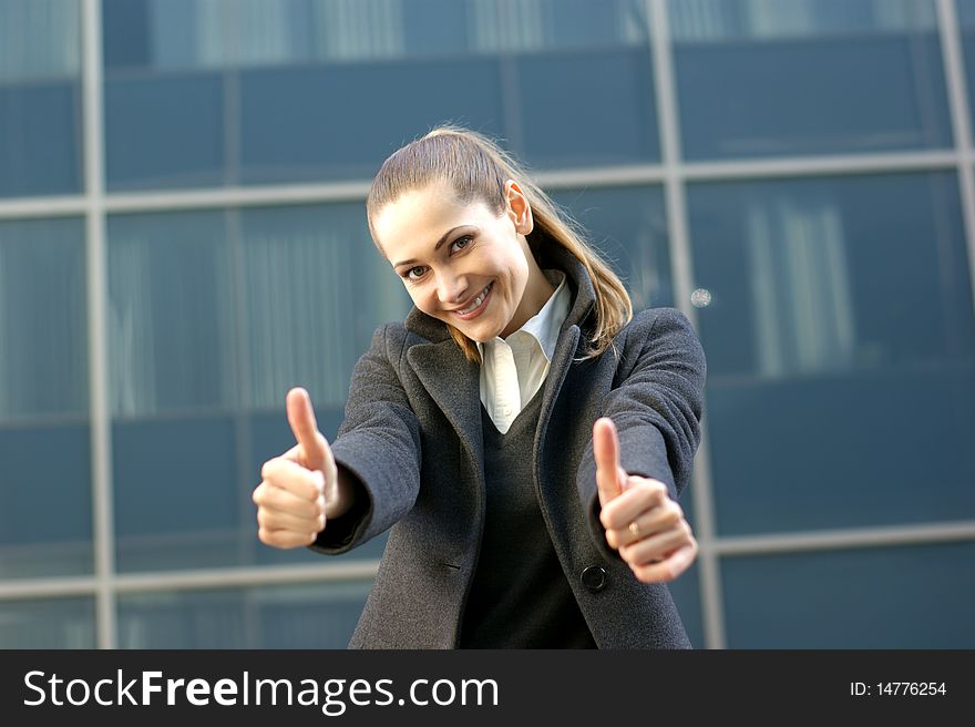 A young and attractive business woman in formal clothes is holding her thumbs up as a sign of success. The image is taken on a modern background. A young and attractive business woman in formal clothes is holding her thumbs up as a sign of success. The image is taken on a modern background.