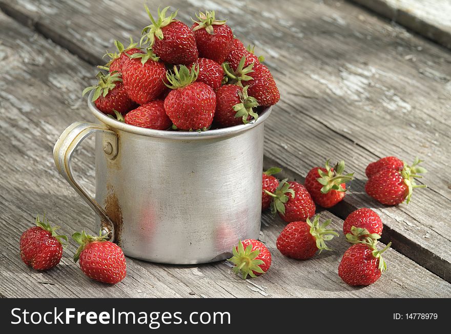 Big aluminum mug full of fresh garden strawberries, stands on the old, wooden table. Big aluminum mug full of fresh garden strawberries, stands on the old, wooden table