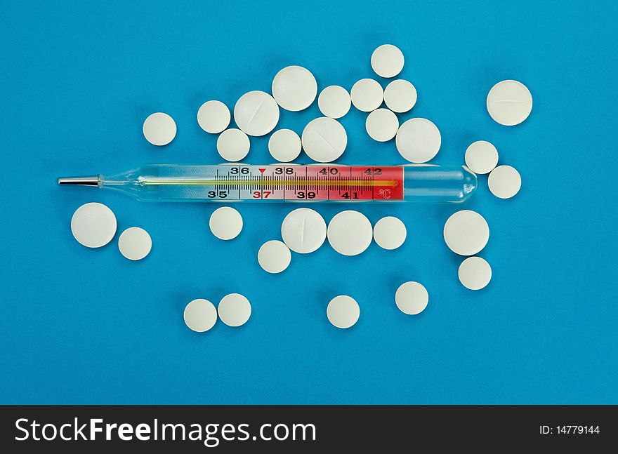 Glass thermometer and white pills on a blue background. Glass thermometer and white pills on a blue background