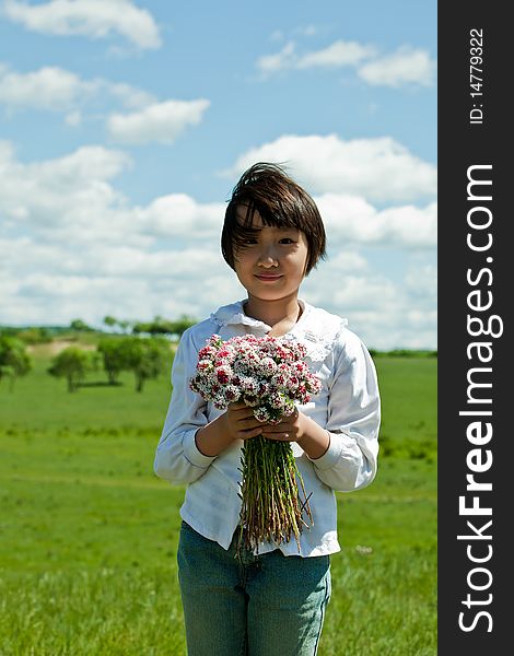 A portrait of a pretty Asian girl, standing on a green pasture and holding a bouquet of fresh beautiful flowers. A portrait of a pretty Asian girl, standing on a green pasture and holding a bouquet of fresh beautiful flowers.