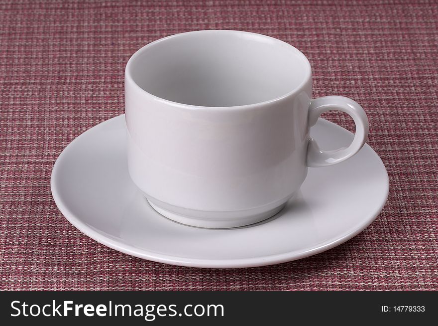 Little white coffee cup on a white saucer over checked table-cloth background