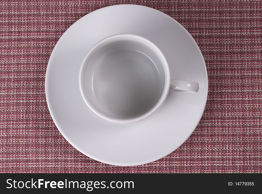 Little white coffee cup on a white saucer over checked table-cloth background