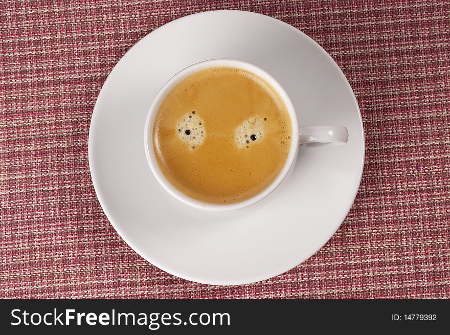 Little white espresso coffee cup on a white saucer over checked table-cloth background (upprer view)