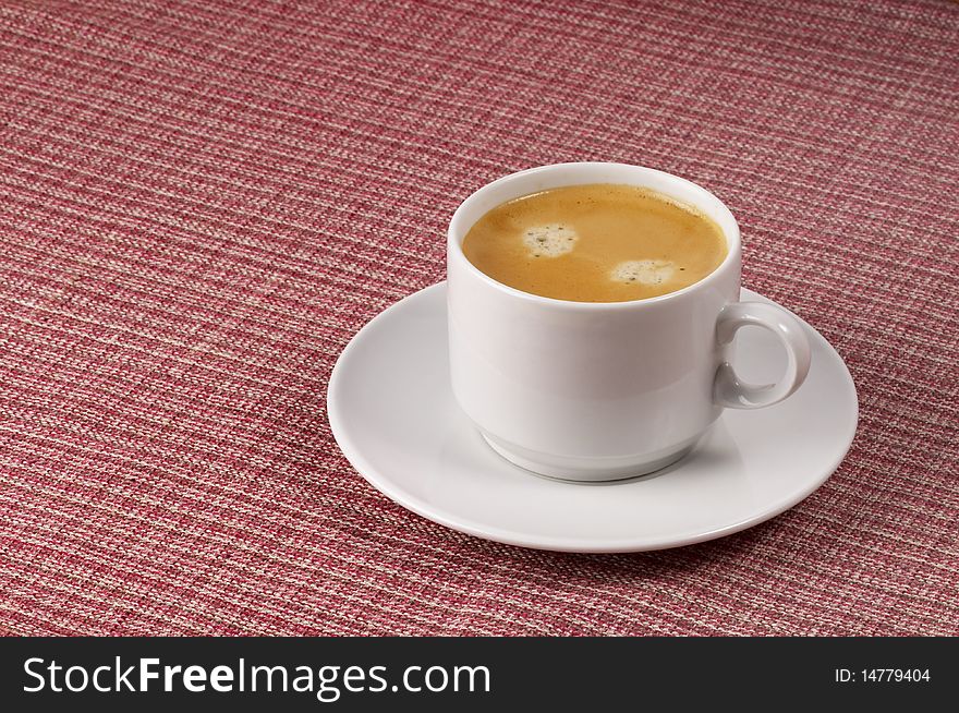 Little white espresso coffee cup on a white saucer over checked table-cloth background