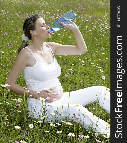 Pregnant woman on meadow with bottle of water