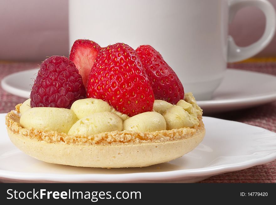 Little white espresso coffee cup and small berry tart over checked table-cloth background. Little white espresso coffee cup and small berry tart over checked table-cloth background