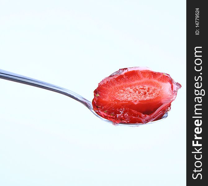 Piece of a strawberriey covered with jelly on a spoon