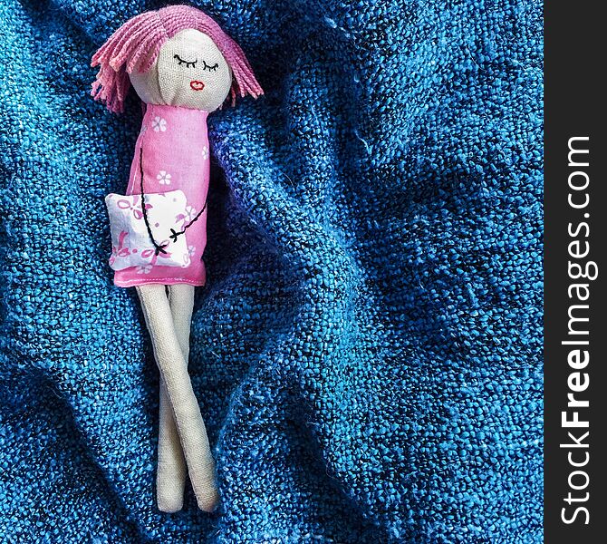 Little sleeping handmade doll made of linen and cotton lying with crossed legs on a blue plaid