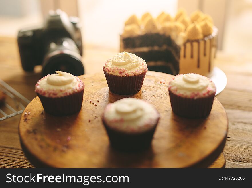 Cupcakes on wooden board with cake and camera on table at the back. Cupcakes on wooden board with cake and camera on table at the back