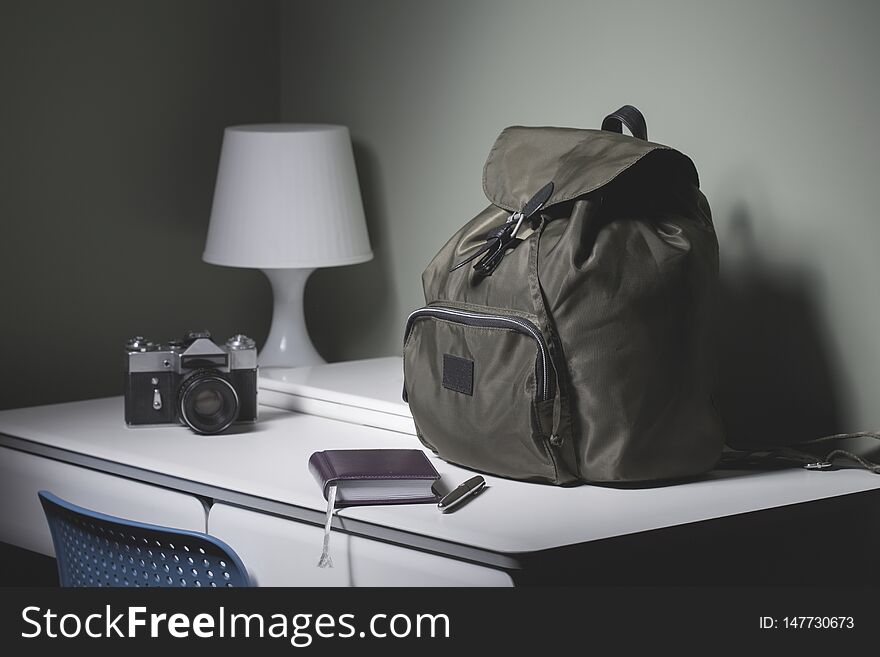 Backpack, camera, laptop, notebook and pen on the desk in the room