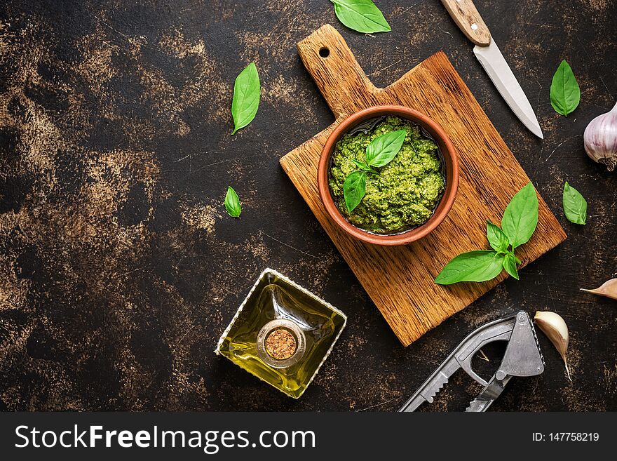 Pesto sauce, basil leaves, garlic and olive oil on a dark rustic background. Overhead view,copy space