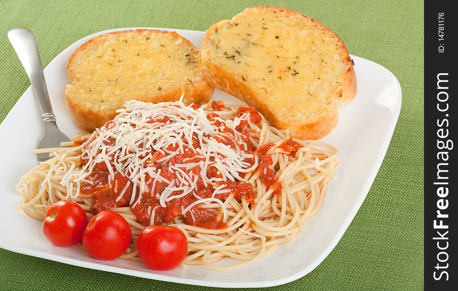 Plate of spaghetti topped with sauce and cheese with garlic toast and cherry tomatoes. Plate of spaghetti topped with sauce and cheese with garlic toast and cherry tomatoes