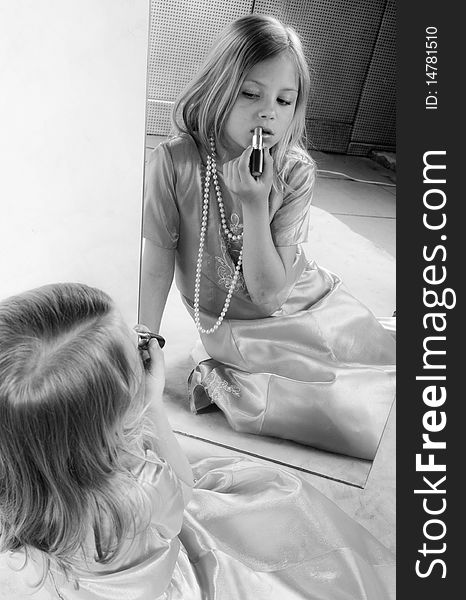 Little girl rouge lips and looking at mirror, studio photo, black and white portrait