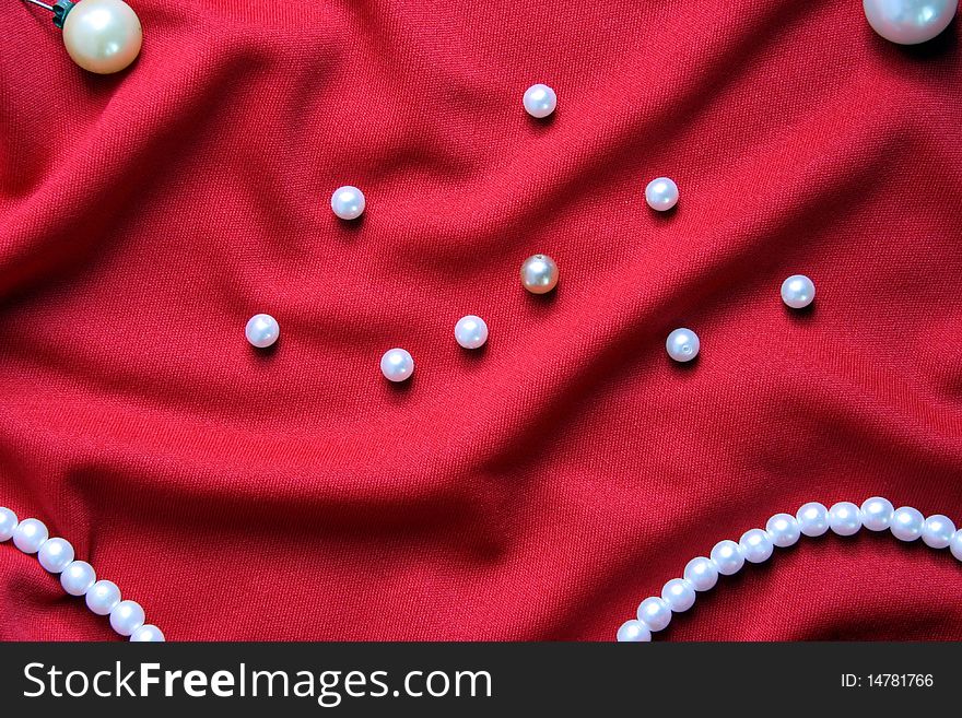 Nacreous pearls and necklace on a red fabric with folds