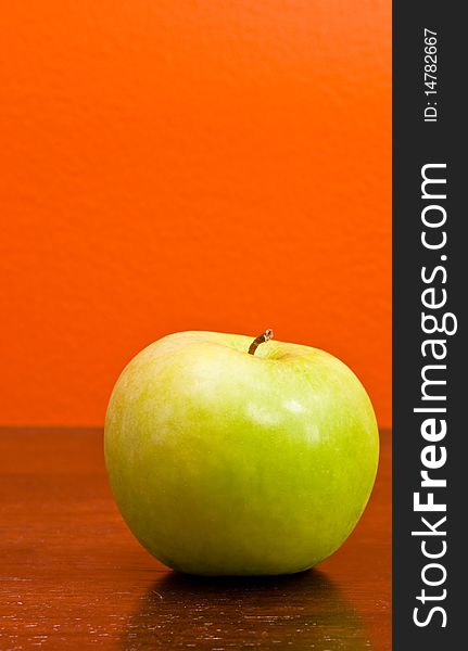 A delicious ripe green apple against an orange background. A delicious ripe green apple against an orange background.