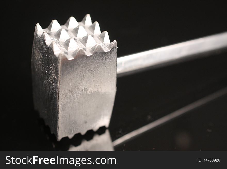 Metal meat tenderizer on a black, reflective surface.