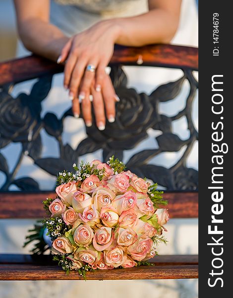 A vertical photo of a rose bouquet resting on a wooden bench, with a caucasian bride leaning behind it. A vertical photo of a rose bouquet resting on a wooden bench, with a caucasian bride leaning behind it