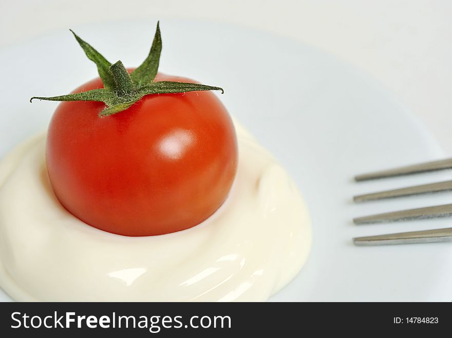 Red cherry tomato with mayonnaise on a saucer and a fork. Red cherry tomato with mayonnaise on a saucer and a fork