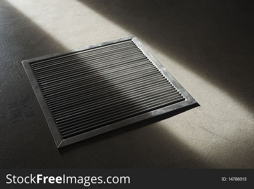 Steel grate in a concrete floor partially lit