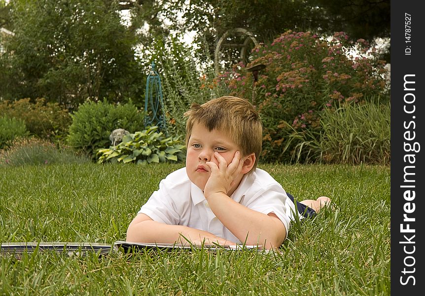 Young boy lays on grass dreaming while reading a book. Young boy lays on grass dreaming while reading a book