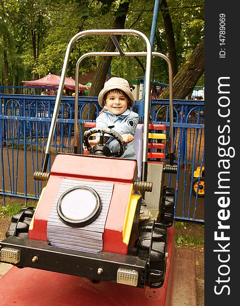 Little joyful boy in hat riding on toy-car on adventure playground, outdoor shot. Little joyful boy in hat riding on toy-car on adventure playground, outdoor shot