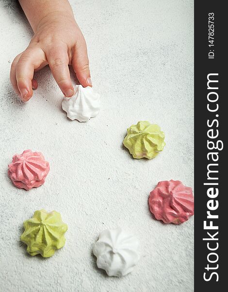 Little baby hand takes a French sweet meringue dessert on a white retro background, vertically.