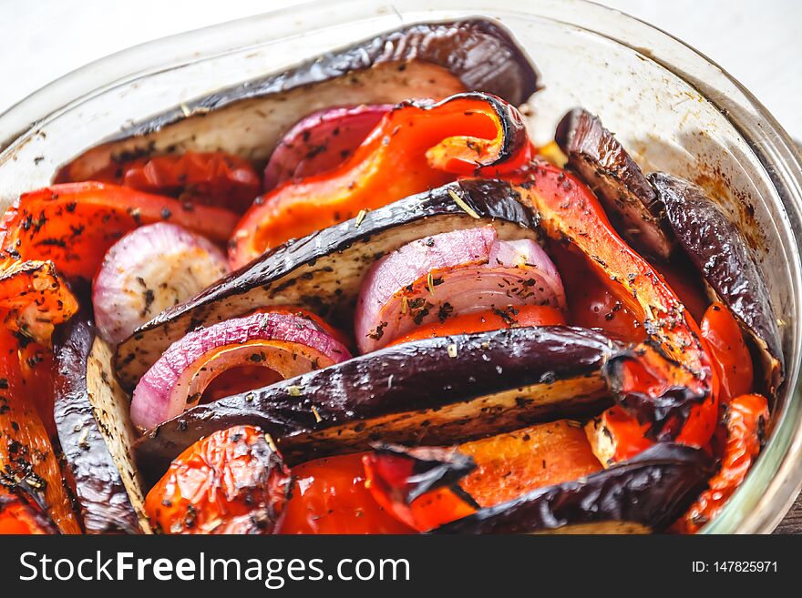 Baked vegetables tomatoes, eggplants, blue onions, zucchini, zucchini in glass form on a bright white background. The concept of