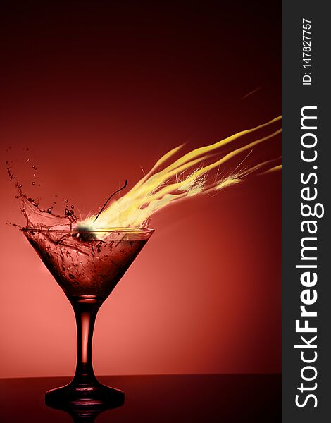 Alcoholic coctail with a flame and a splash on red background