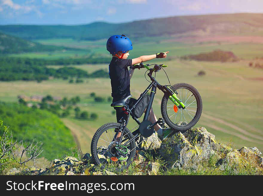 Little child stand next to his mountain bike on mountains edge and looks at the beautiful scenery