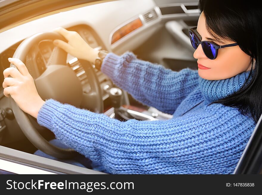 A beautiful pretty brunette woman in a blue sweater and sunglasses is driving a car. Toned