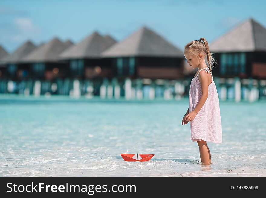 Adorable little girl playing with origami boat in turquoise sea. Adorable little girl playing with origami boat in turquoise sea