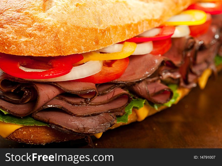 Large roast beef sandwich with cheese, lettuce, tomatoes, onion, red and yellow peppers.