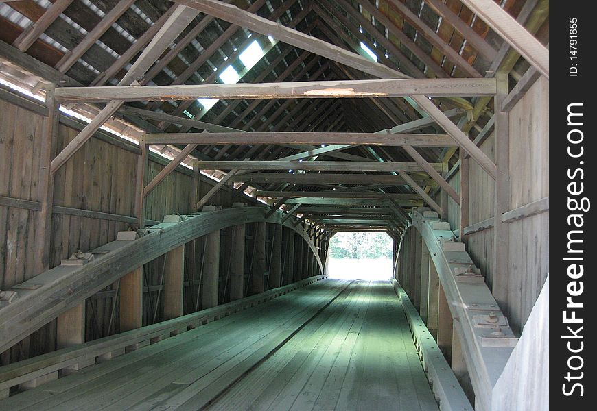 Standing inside a long single span covered bridge. The arch support on both side with rods going thru and connecting thru the floor. The beams and truss forms along the top and sides add support. Standing inside a long single span covered bridge. The arch support on both side with rods going thru and connecting thru the floor. The beams and truss forms along the top and sides add support.