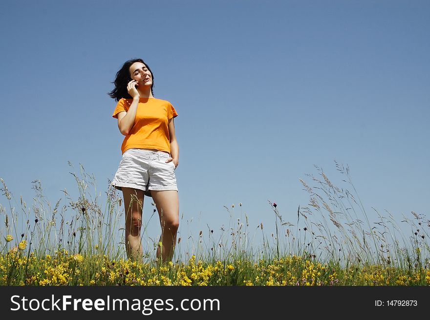 Happy woman enjoying the outdoors using her cell phone in orange T-shirt