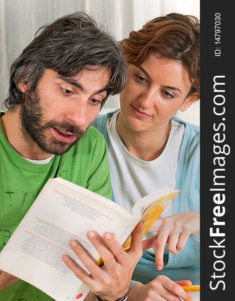 A young couple are sitting down reading a book together. The book is yellow and their clothing is pastel blue and green. A young couple are sitting down reading a book together. The book is yellow and their clothing is pastel blue and green.