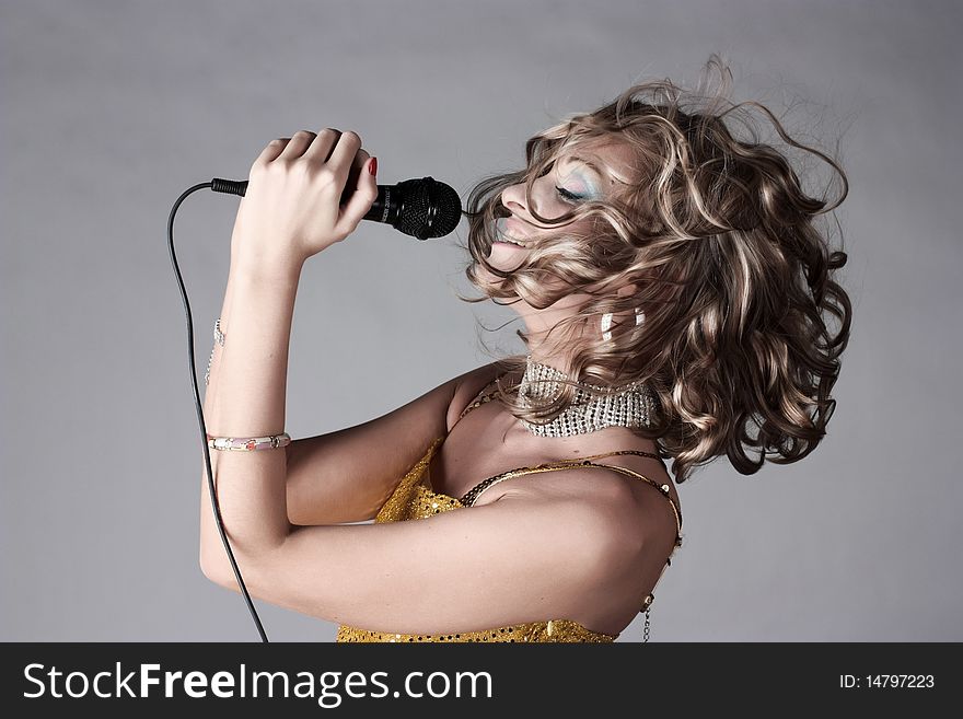 Beautiful girl in trend clothes holding microphone and singing. Beautiful girl in trend clothes holding microphone and singing